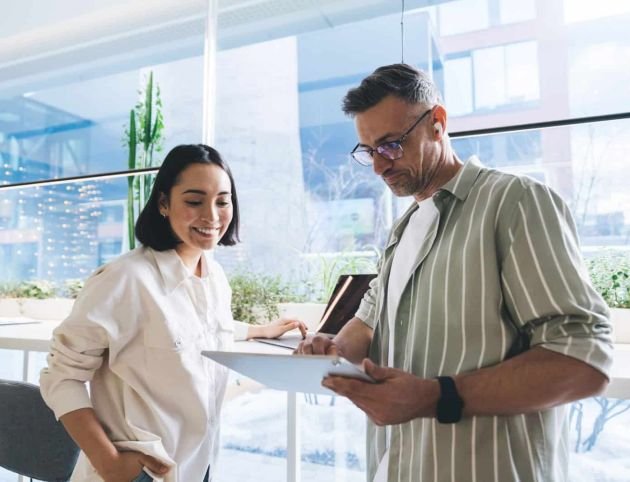 Asian and Caucasian colleagues with touch pad device talking about business marketing in coworking space, successful skilled male and female entrepreneurs with digital tablet browsing web and smiling